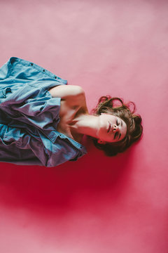 Young woman wrapped in denim lying on a pink background