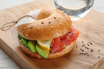 Tasty bagel sandwich with salmon and lemon on wooden board
