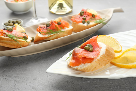 Tasty small sandwiches with salmon and capers on plates