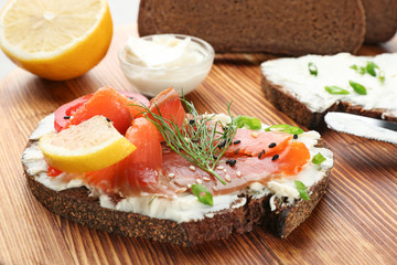 Tasty sandwich with salmon and creamy cheese on wooden background