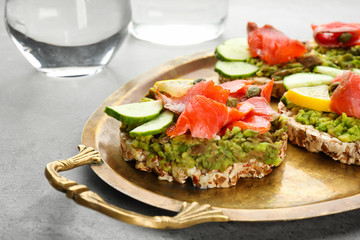 Tasty crispbread sandwiches with salmon and avocado on metal dish