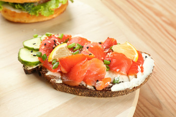 Tasty sandwich with salmon and creamy cheese on wooden board