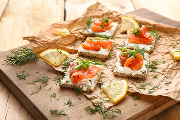 Tasty crispbread sandwiches with salmon and creamy cheese on wooden board