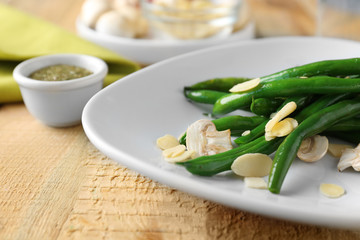 Plate with delicious green beans, almond and mushrooms on table