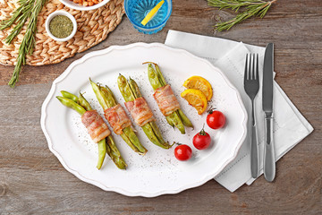 Plate with delicious bacon-wrapped green beans on table