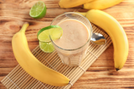 Banana smoothie in glass decorated with slice of lime on wooden table