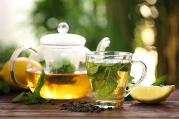 Teapot and cup with tasty mint tea on table