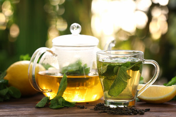 Teapot and cup with tasty mint tea on table