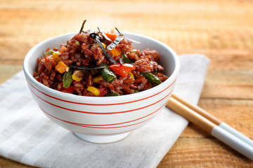 Bowl with brown rice and vegetables on wooden table
