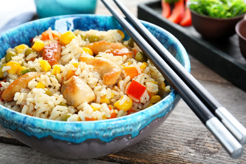 Bowl with brown rice, vegetables and chopsticks on table