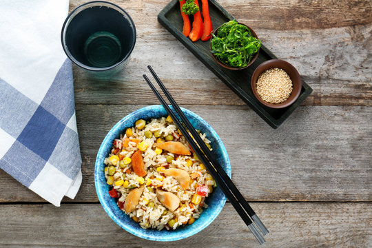 Bowl with brown rice, vegetables and chopsticks on table