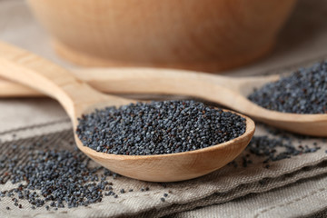 Ripe poppy seeds and wooden spoons on fabric