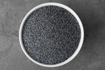 Ripe poppy seeds in ceramic bowl on grey background