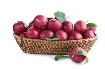 Wicker basket with ripe plums on white background