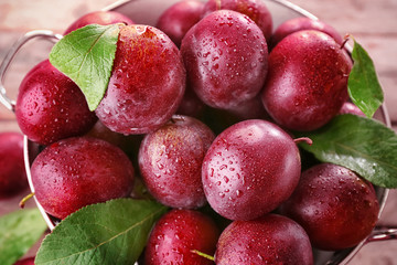 Colander with fresh ripe plums on table