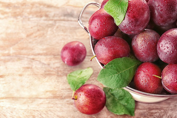 Colander with fresh ripe plums on table