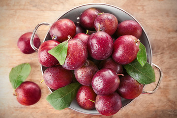 Colander with fresh ripe plums on table