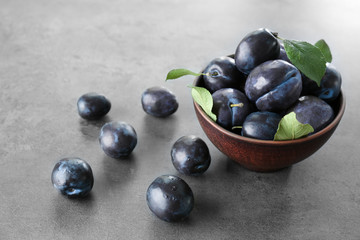 Bowl and ripe plums on table