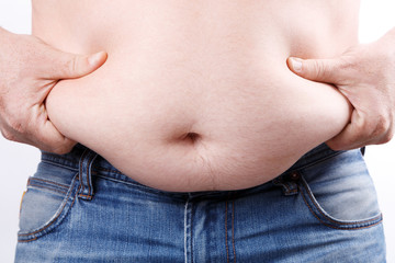 Guy shows with his hands his fat folds on his belly closeup. Overweight caucasian man in blue jeans...