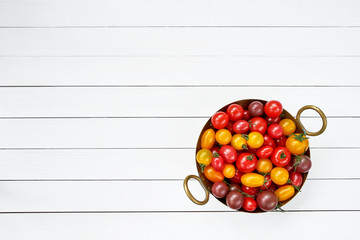 Colorful tomatoes in colander on white wooden table. Top view, copy space