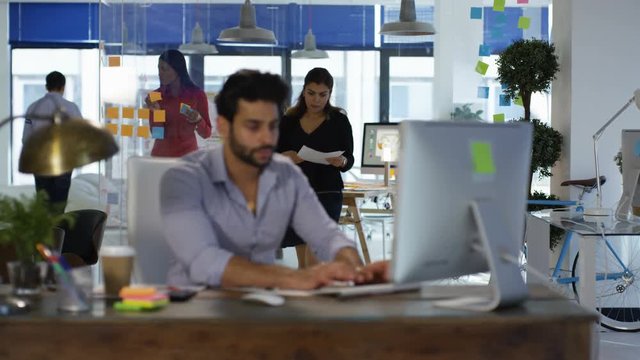 Designer working at his desk in creative office and talking to female colleague.