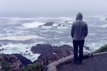 Lonely man standing in front of the pacific ocean and looking at the stormy sea on Vancouver Island.