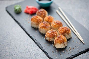 Japanese cuisine. Baked (hot) sushi with crab meat and cheese on a stone slab on a black granite background. Top view with copy space