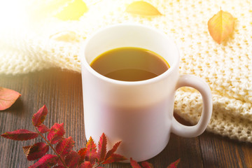 Mug of hot coffee in autumn setting on a wooden table with a knitted scarf, sweater. Comfort, warmth, cozy.