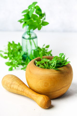 Green lemon basil in a wooden mortar on a light background. Behind the basil in the bottle.