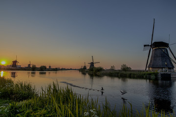 Fototapeta na wymiar Travelling Concepts and Ideas. UNESCO Heritage Dutch Windmills In Front of The Canal and Sun at Kinderdijk Located in Traditional Village in Holland, The Netherlands