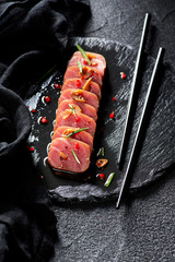 Tuna steak in oil with chilli and rosemary on black slate plate