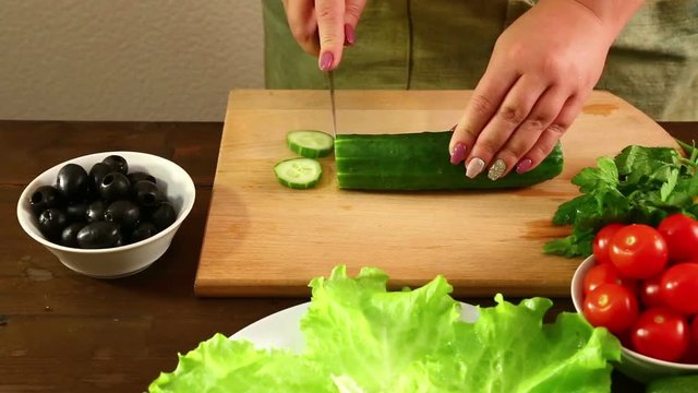 Female hands cut a cucumber to make a vegetable salad. Shot with dolly from from left to right