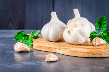 Garlic cloves and garlic bulb on a wooden board on a gray background.