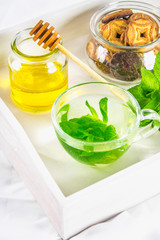 Mint tea in a cup, a jar of honey, a cookie in a jar, on a white tray in bed.