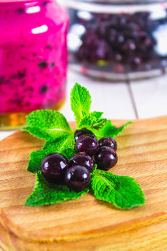 Black currant on a blackboard with a straw and smoothies on a white wooden table.