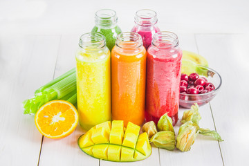 Multicolored smoothies in bottles of mango, orange, banana, celery, berries, on a wooden table.