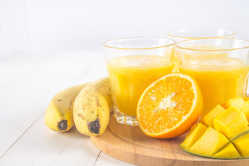 Yellow smoothie of mango, banana and orange on a white wooden table.
