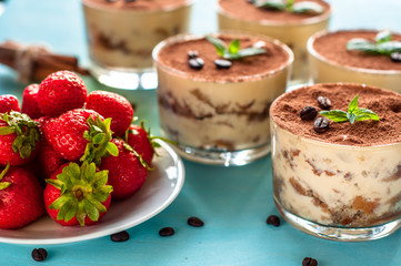luxurious dessert Tiramisu in a glass on a blue background decorated with mint and strawberries