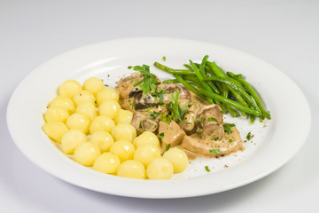 Pork tenderloin with potatoes and wild mushroom sauce and green beans on white plate