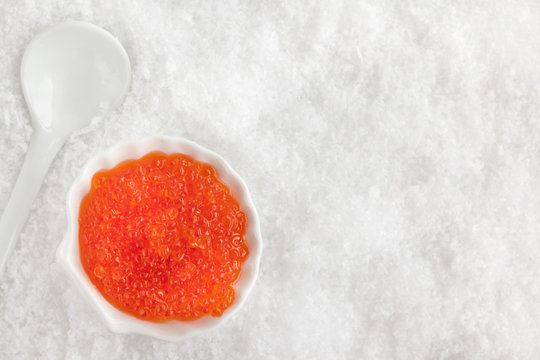 Delicious red caviar in bowl on white snow background
