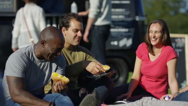  Happy friends chatting & eating fast food from burger van at community event