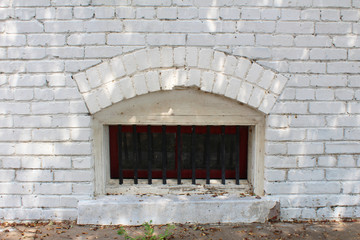 Small arched basement window with bars in a white brick wall

