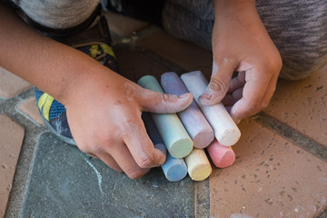 Child holding a bunch of large colorful chalks on the ground © Neeqolah