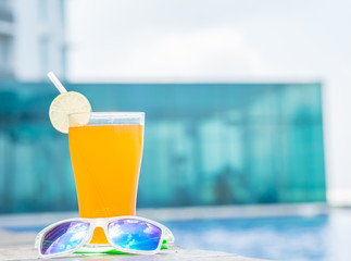 Sunglasses with orange juice and a piece of lemon at the side of swimming pool. Vacation, beach, summer travel concept