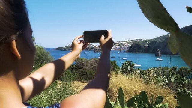 Young Woman taking pictures of the sea with her smartphone on Ponza Island Italy