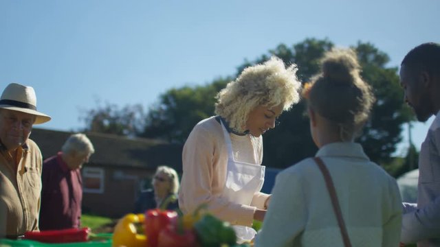  Cheerful woman selling fresh fruit & veg to customers at summer market