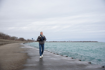 Young man is walking on the sidewalk in the park near lake