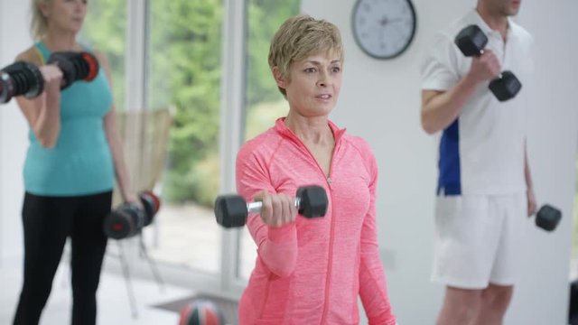  Mature fitness instructor working out & lifting weights with 2 clients in gym