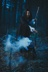 Halloween Young beautiful and mysterious woman witch in woods, in black cloak with hood, witch...