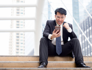 Asian businessman happy while using smart phone/cell phone receiving good news about successful about business